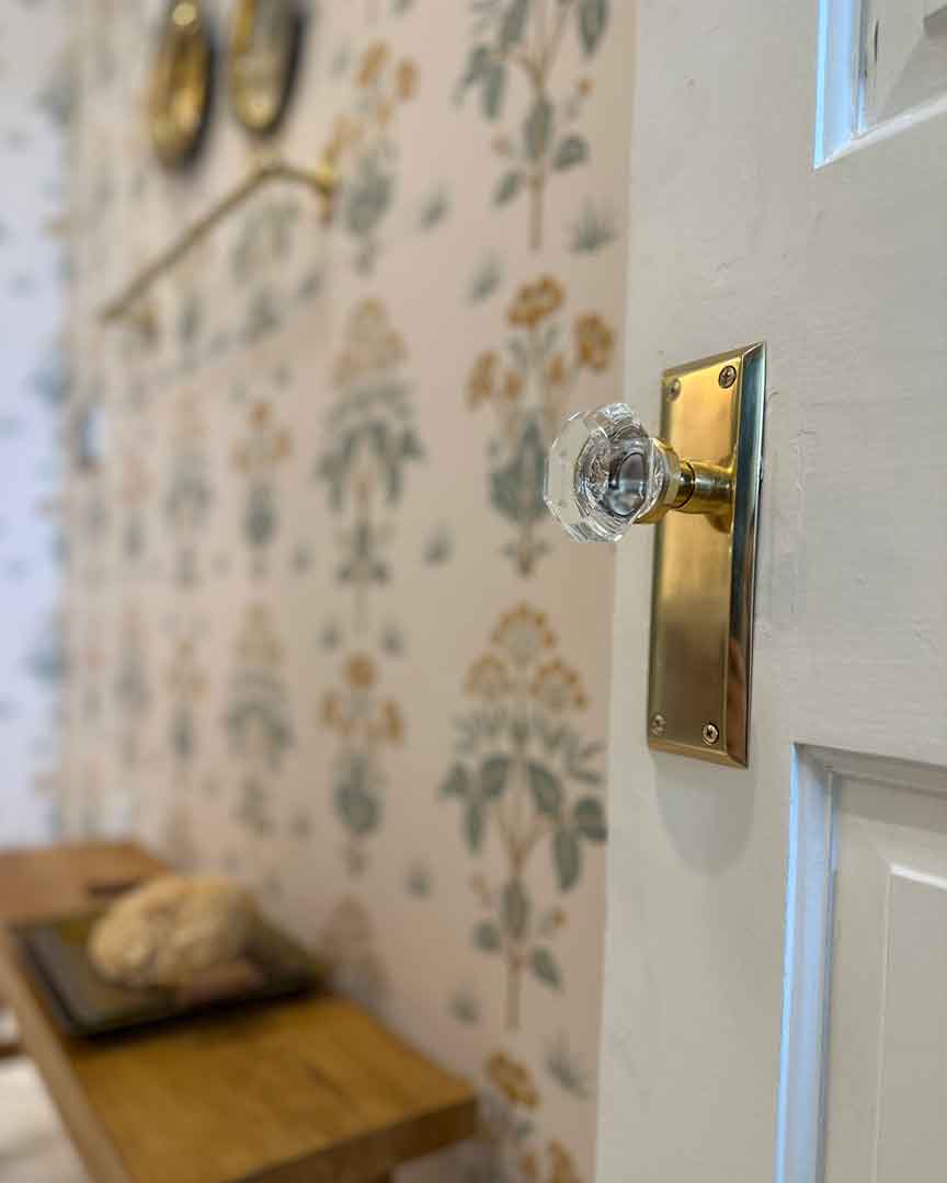 Crystal knob on an unlacquered brass long plate against floral wallpaper at Swell Stay in Madison, Indiana, Nostalgic Warehouse